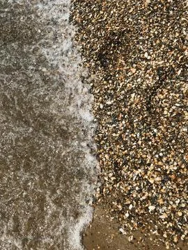 Waves gently washing over a shell strewn beach shore 写真素材