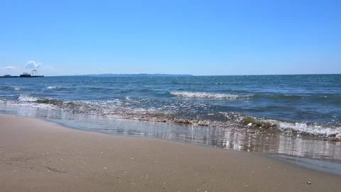 Waves Gently Washing Onto a Sandy Beach Under Bright Blue Sky Stock Footage 310233051