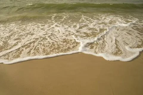Waves gently washing onto sandy beach shoreline Stock Photos