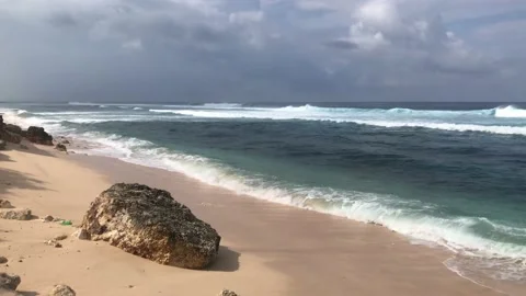 The waves hit a large black rock on the beach, the beach sand is clean and soft Vidéo 199762951