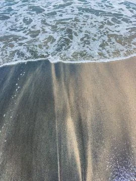 Waves hit the shore and create patterns on the sand at the beach in the aft.. Fotos Stock