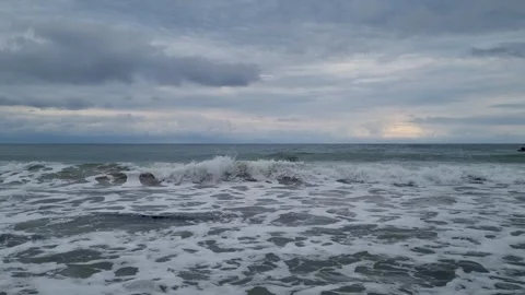 Waves hitting beach shore under dramatic cloudy sky at sunset horizon Stock Footage 319985075