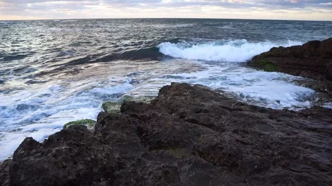 Waves hitting rocky cliff horizontal view as sunsets down Stock Footage 95979126