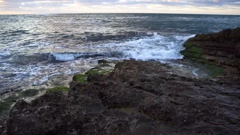 Waves hitting rocky cliff as sunsets down Stock Footage 95979029