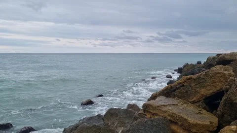 Waves hitting rocky coastline under cloudy gray sky in Varna Stock Footage 320134239