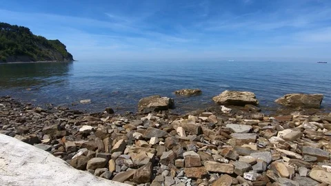 Waves hitting rocky pebble shore on bright sunny day Stock Footage 130073531