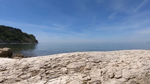 Waves hitting rocky pebble shore on bright sunny day Stock Footage 130073549