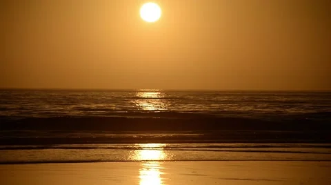 The waves hitting the shore with the bridge made by the setting sun Stock Footage 44782603