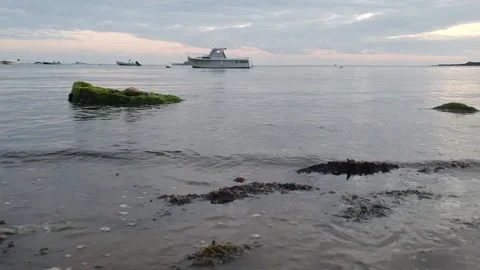 Waves hitting the shore with a rock and seaweed and a boat in the background Stock Footage 161325561