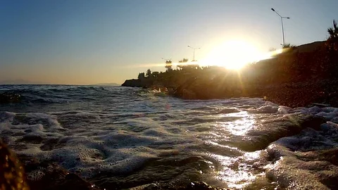 Waves hitting the shore at sunset Stockbeeldmateriaal 104434801