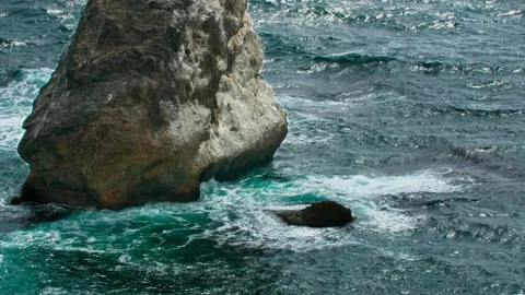 Waves hitting a stone pillar rising in the coastal zone of the sea. Long shot Stock Footage 217730844