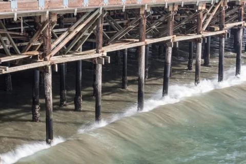 Waves just beginning to break against wood pilings of an ocean pier Stock Photos