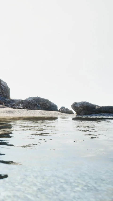 Waves lap against rocks on a quiet beach during early morning light Video stock 342178862