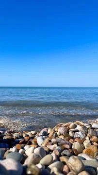 Waves lap against smooth pebbles on a sunny day by the sea with clear blue .. Stock Photos