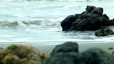 Waves lap volcanic rock on a sandy beach Stock Footage 89702471