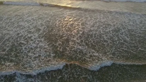 Waves lapping on beach with sunrise and surfers sitting in the water Stock Footage 79212198