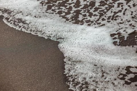 Waves lapping on the black sand Stock Photos