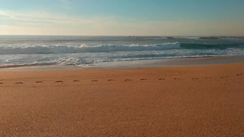 Waves lapping on sandy beach with human footprints in sand in foreground Stock Footage 103065600