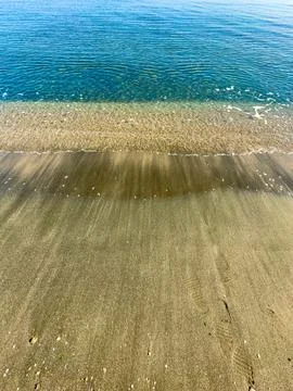 Waves meet sand at a beach during a sunny day with clear skies and calm water Stock Photos