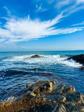 Waves move over rocks as they meet the shoreline during the afternoon. The sk Fotos de archivo