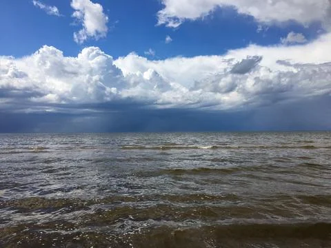 Waves move slowly under a blue sky filled with clouds over a calm ocean dur.. Stock Photos