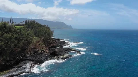 The waves of the ocean foam and run to the stone shore with the forest at Kauai Video stock 135950829