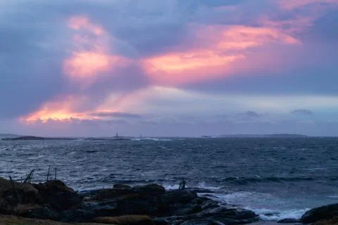 Waves from ocean hitting rocks with clouds an sunset Stock Photos