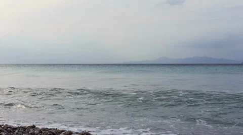Waves on a pebble beach in the evening cloudy with cruise ship and the mountains 스톡 동영상 65581493