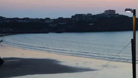 Waves ripple onto the golden sandy beach as people stroll at dusk 動画素材 85739401
