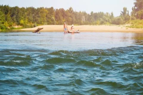 Waves on the river roll, unrecognizable people walk on the water in the distance 스톡 사진