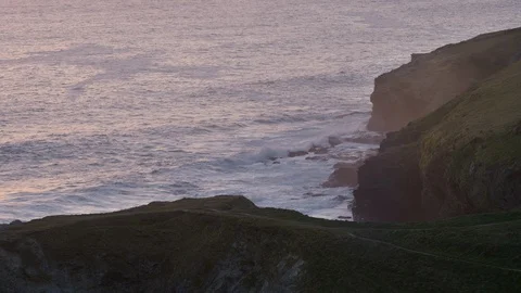 Waves roll in and break along cliff at sunset in Cornwall, England. Stock Footage 128214388