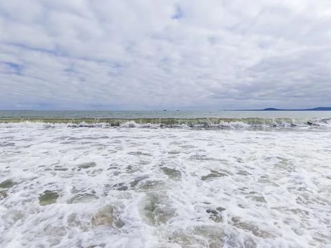 Waves roll in and break on the shore as clouds cover the sky. The scene shows Stock Photos
