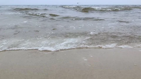 Waves roll ashore leaving foam behind. The gray landscape and horizon create a s Stock-Footage 120627692