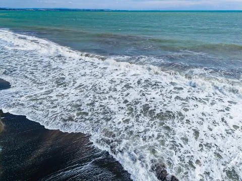 Waves roll onto a dark sand beach at a coastline during a cloudy day with s.. Stock Photos