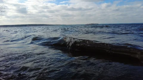 Waves roll on a lake shore with clouds in the sky on a cool day in late autumn Vídeos de archivo 332635432