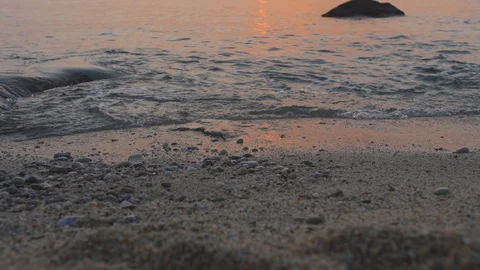 Waves roll on sand and pebble stones on a sea shore. Water reflects sunset light Stock Footage 102458085