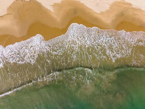Waves roll onto the sandy shore at a beach during daylight with clear blue .. Stockfoto's