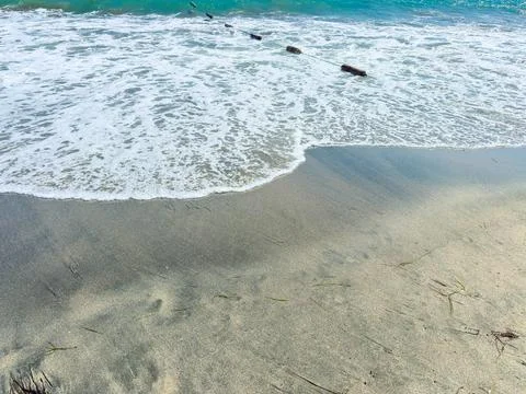Waves roll onto a sandy shore, leaving foam and moving small pieces of wood.  Stock Photos