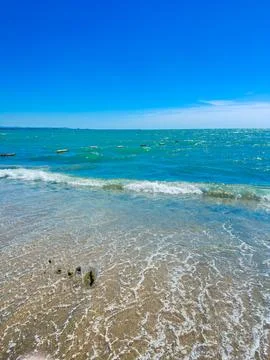 Waves roll onto the sandy shore while sunlight reflects off the water. A few  Foto stock