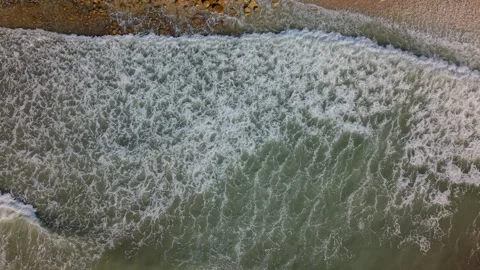 Waves roll onto the shore at a beach during the afternoon in a coastal region Stock Footage 346017694
