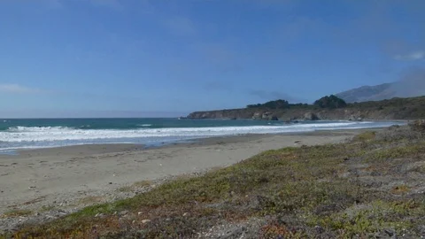 Waves roll into shore onto sand on empty beach with rocks and cliff B Stock Footage 125341412