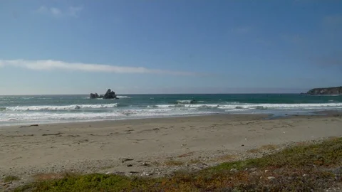 Waves roll into shore onto sand on empty beach with rocks and cliff A Stock Footage 125341416
