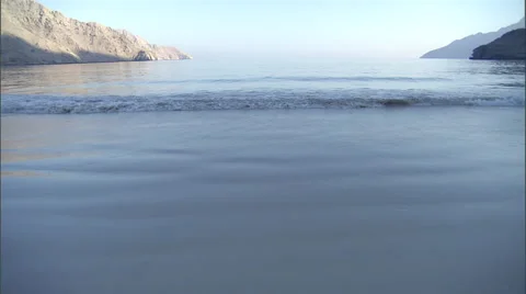 Waves roll onto the shore, situated near moutain ranges. Video stock 46868346