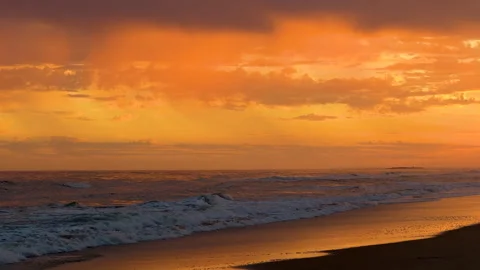 Waves roll in under a vibrant, dramatic sky painted with deep sunset hues. Stock Footage 291333140