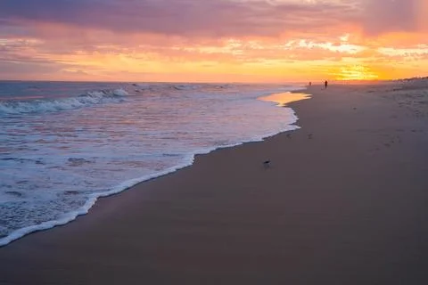 Waves roll in under a vibrant, dramatic sky painted with deep sunset hues. Stock Photos
