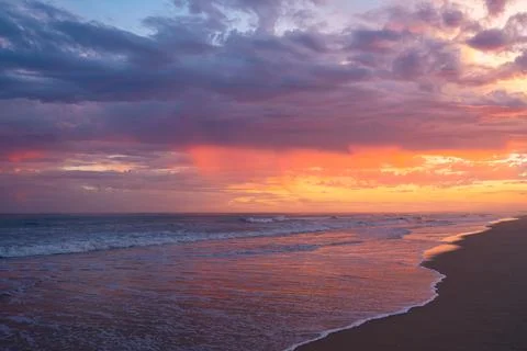 Waves roll in under a vibrant, dramatic sky painted with deep sunset hues. Foto stock