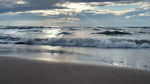 Waves roll on wet sandy beach in sunset lighting and clouds reflects in water Stock Footage 161840865