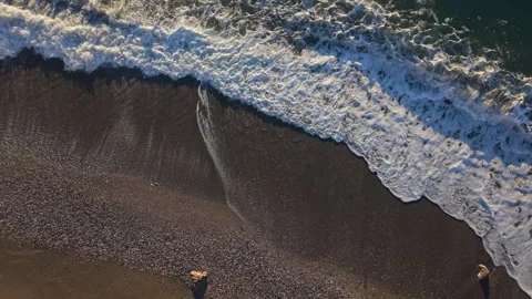 Waves rolling ashore on sandy beach with rocky shoreline.Overhead low rising Stock Footage 341111420