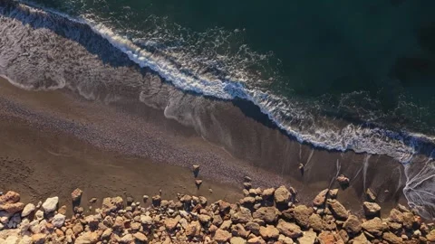 Waves rolling ashore on sandy beach with rocky shoreline.Overhead rising drone Stock Footage 341112063