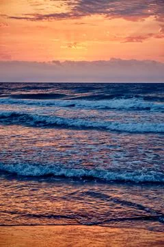 Waves rolling on the beach during sunset with vibrant colors in the sky and.. Stock Photos